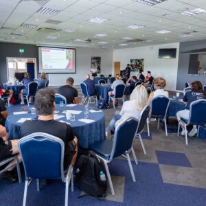 View of the networking room - tables laid out with attendees sat listening intently to the presentations