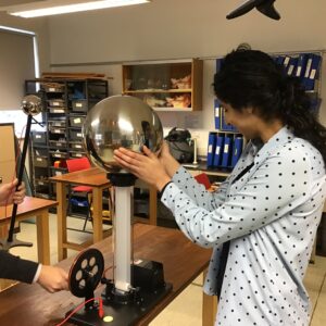 Female student with both hands around the electrically charged dome on the Van de Graaff generator