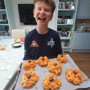 Male student with a tray of orange rice krispie cakes, smiling