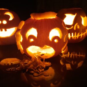 Three carved pumpkins, each boasting a different creepy face, lit up in the dark with tealights