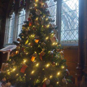 Close up of Christmas Tree with warm white twinkly lights and named baubles. A stain glass window can be seen in the background