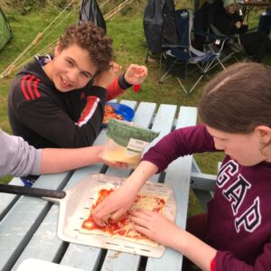 Students sat on a picnic bench at their camp putting toppings on their own pizzas