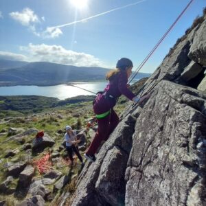 Female student mid-rock climb with beautiful welsh scenery in the background (mountains and water) on a bright sunny day