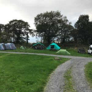 Campsite comprising of three green tents, two blue and a green shelter. The NCW minibus is parked alongside