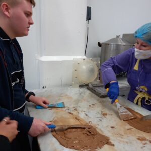 Male VI student scraping tempered chocolate across the work surface