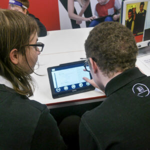 Two male students are working together, looking at the Optelec Compact tablet