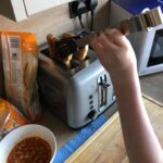 Student is taking toast out of toaster with rubber tongs