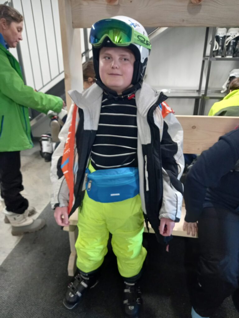 Student Laswon with his ski gear on - bright yellow trousers, grey and black coat,. blue waist bag and helmet with goggles on