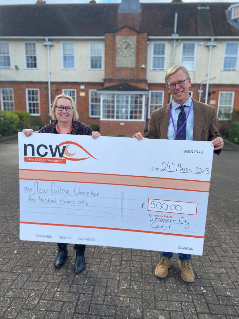 Image of Councillor Piotrowski and Mrs Madden holding a giant cheque outside of NCW. The clock tower is in the distance