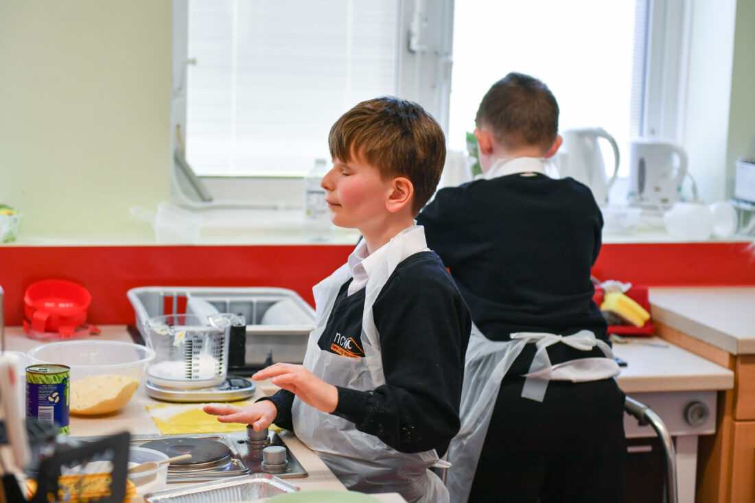 image of a student wearing an apron in a cookery lesson listening to instructions