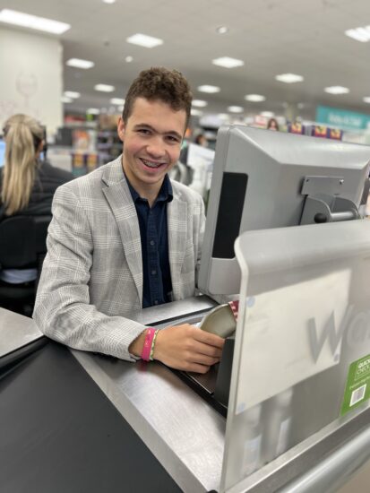 image of Thomas smiling whilst sat behind the checkout