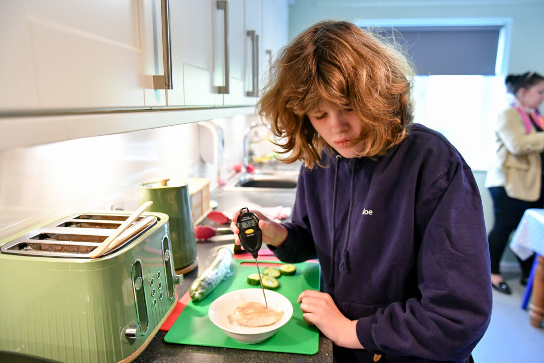 image of a student cooking independently in a lower school house. they are also using a thermometer