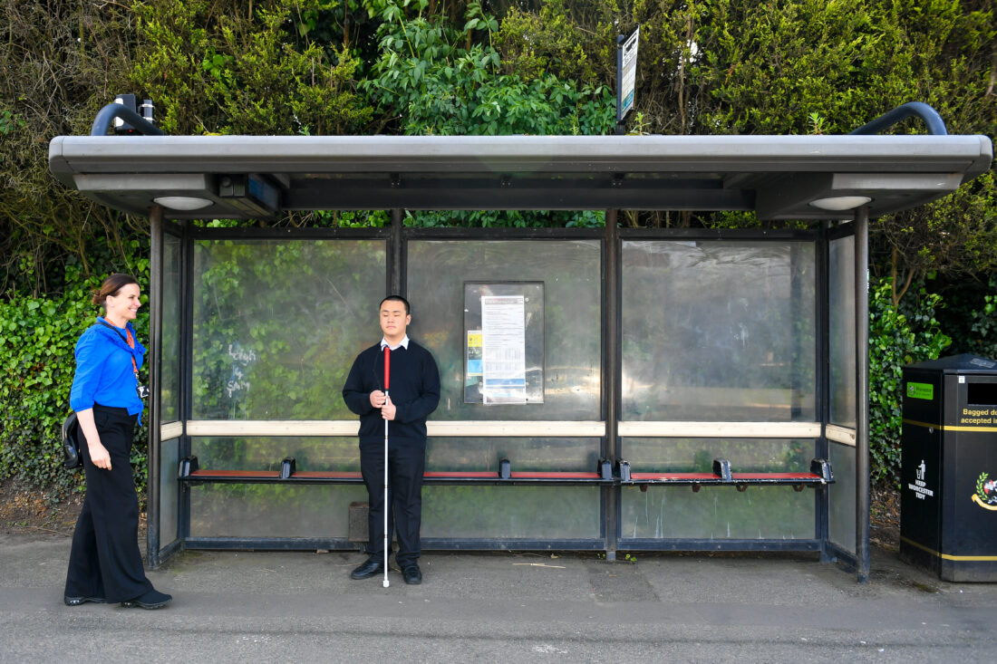 image of a student stood at a bus stop with a Mobility Officer