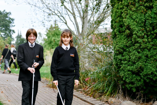 image of two students walking along a path smiling whilst cane trailing 