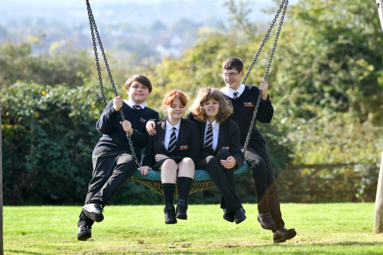 image of four students sat on a swing chatting and laughing