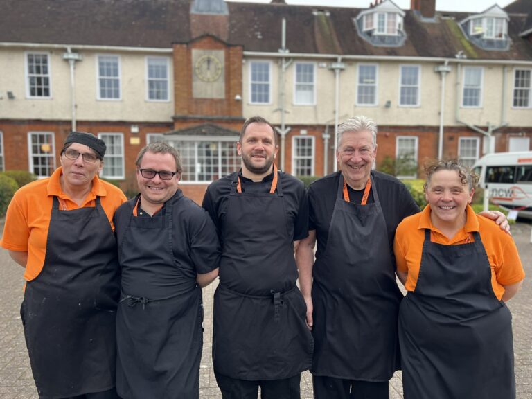 Group photo of all members of the catering team stood outside the main school building smiling