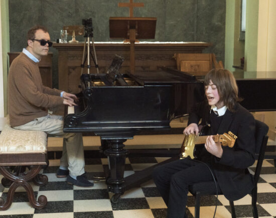 image of Derek sat at the piano playing whilst a student is singing and playing the electric guitar