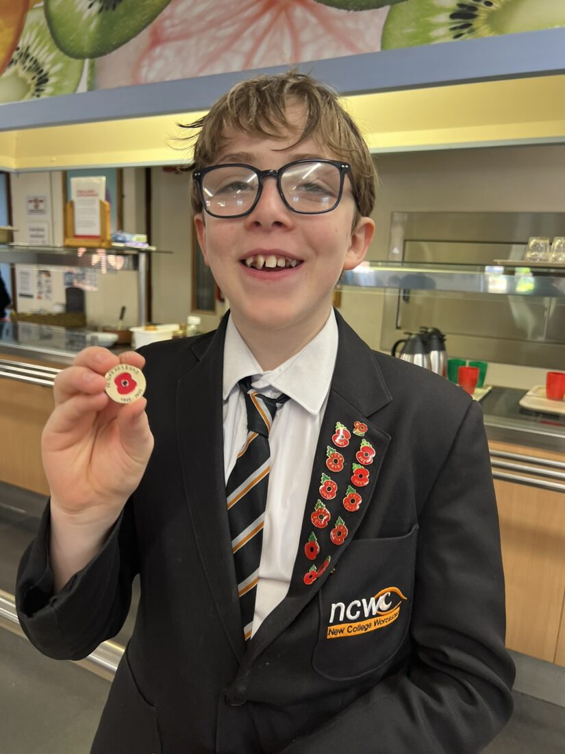 Photo of Zaki smiling whilst holding his new badge. His current poppy badges are on his blazer lapel