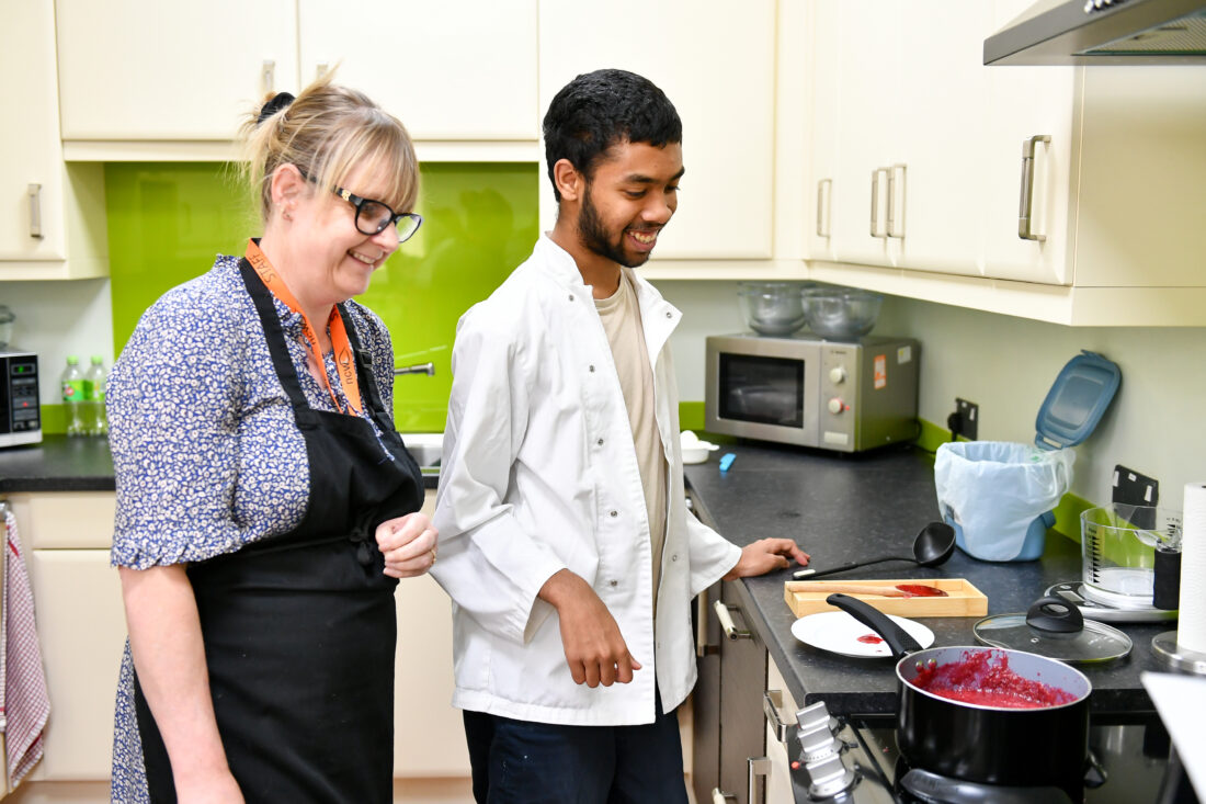 Photo of a student and staff member smiling whilst making jam