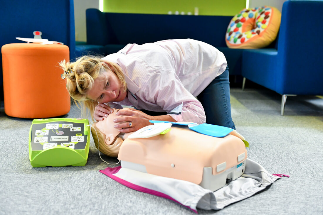 First aid training, woman practicing how to check if a patient is breathing on a dummy.