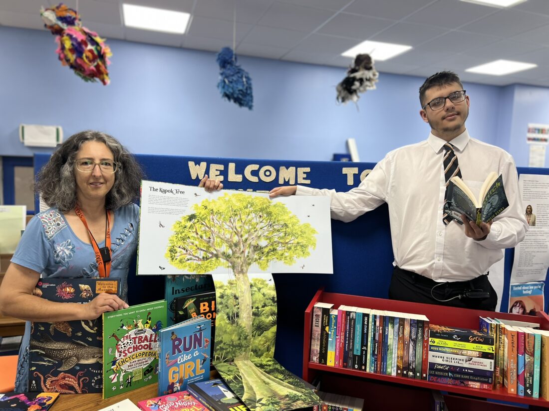 Photo of a student and staff member smiling whilst stood next to the new books
