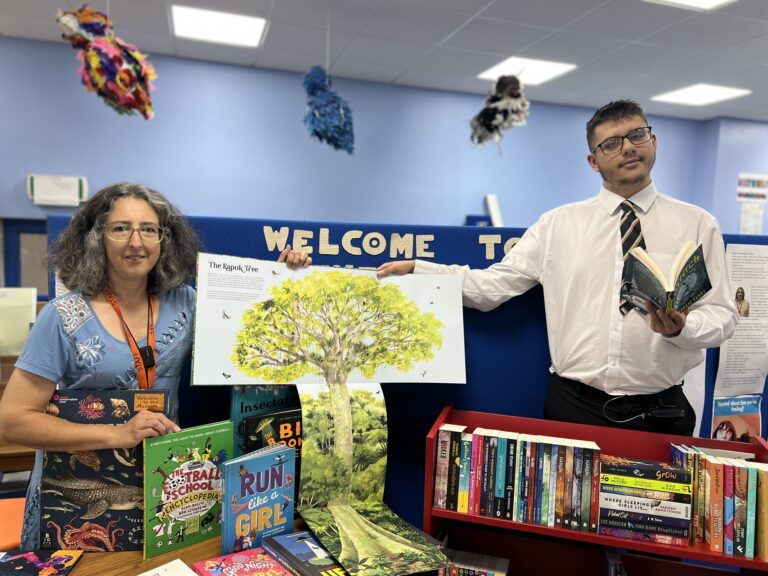 Photo of a student and staff member smiling whilst stood next to the new books