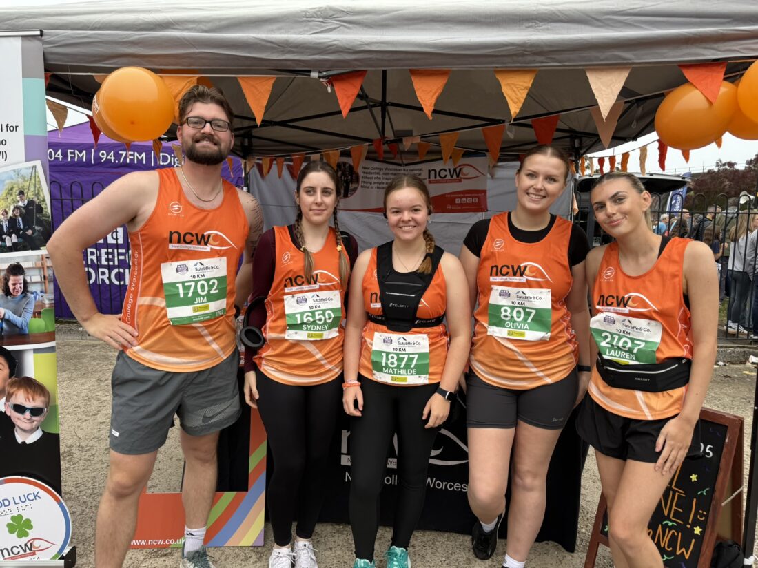 A group of 5 runners smiling for a group photo. They are wearing orange NCW running vests.