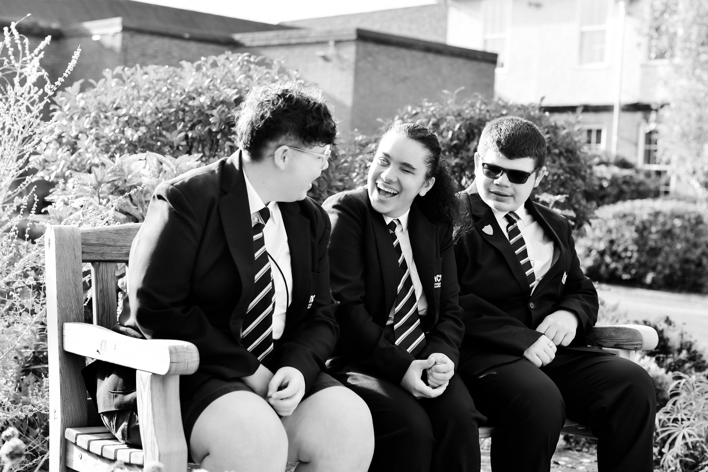 Photo of three students sitting on a bench smiling and talking