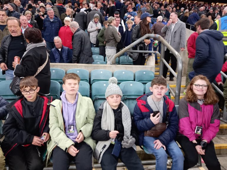 Five students on front row seats in the stadium waiting for the match to start.