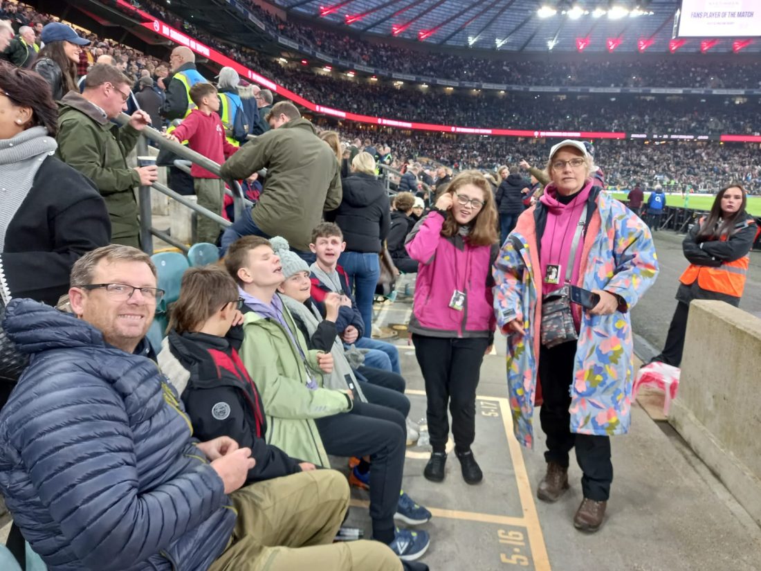 Staff and student on front row seats in the stadium smiling at the camera waiting for the match to start.