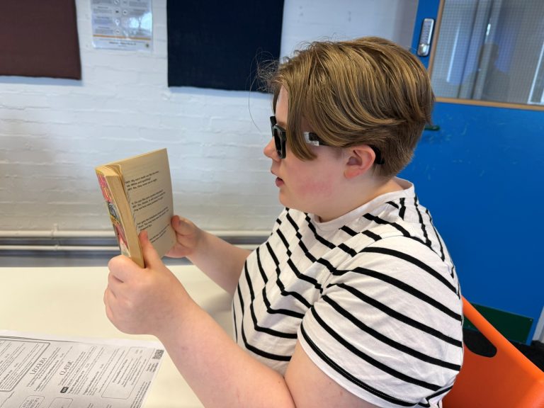 A student wearing the glasses and looking at a book