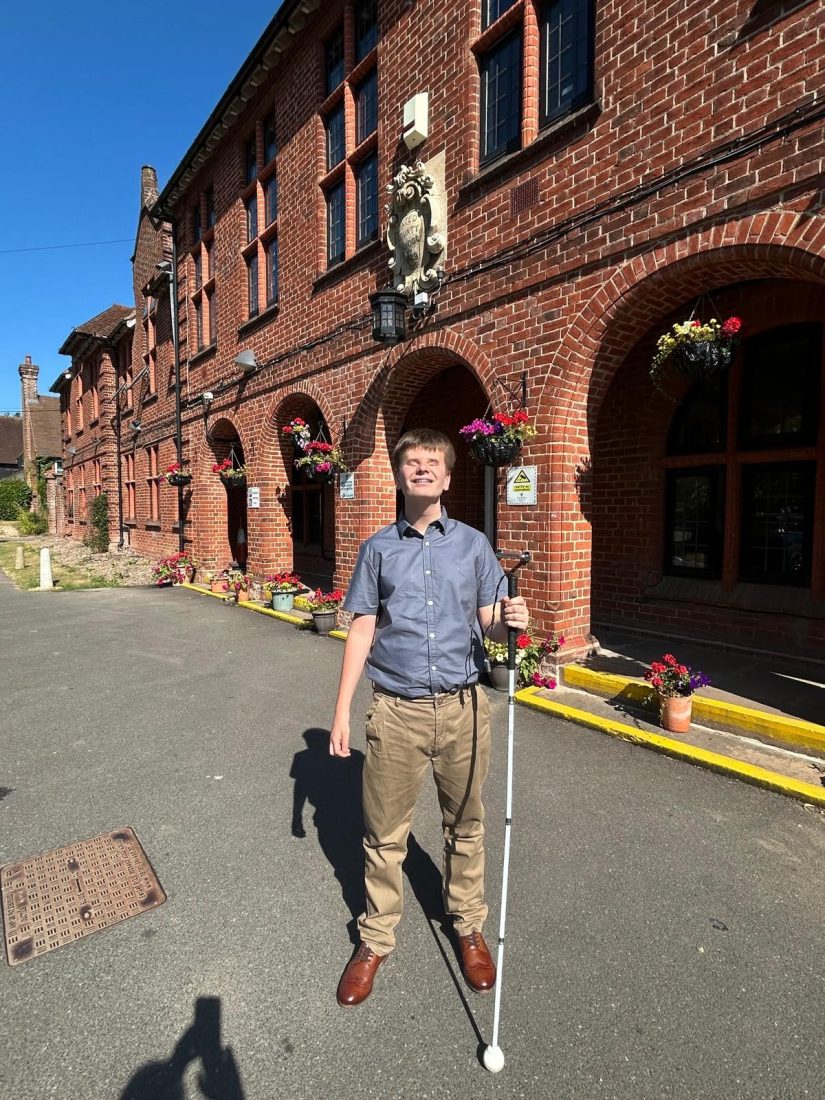 George standing outside the school smiling holding his cane
