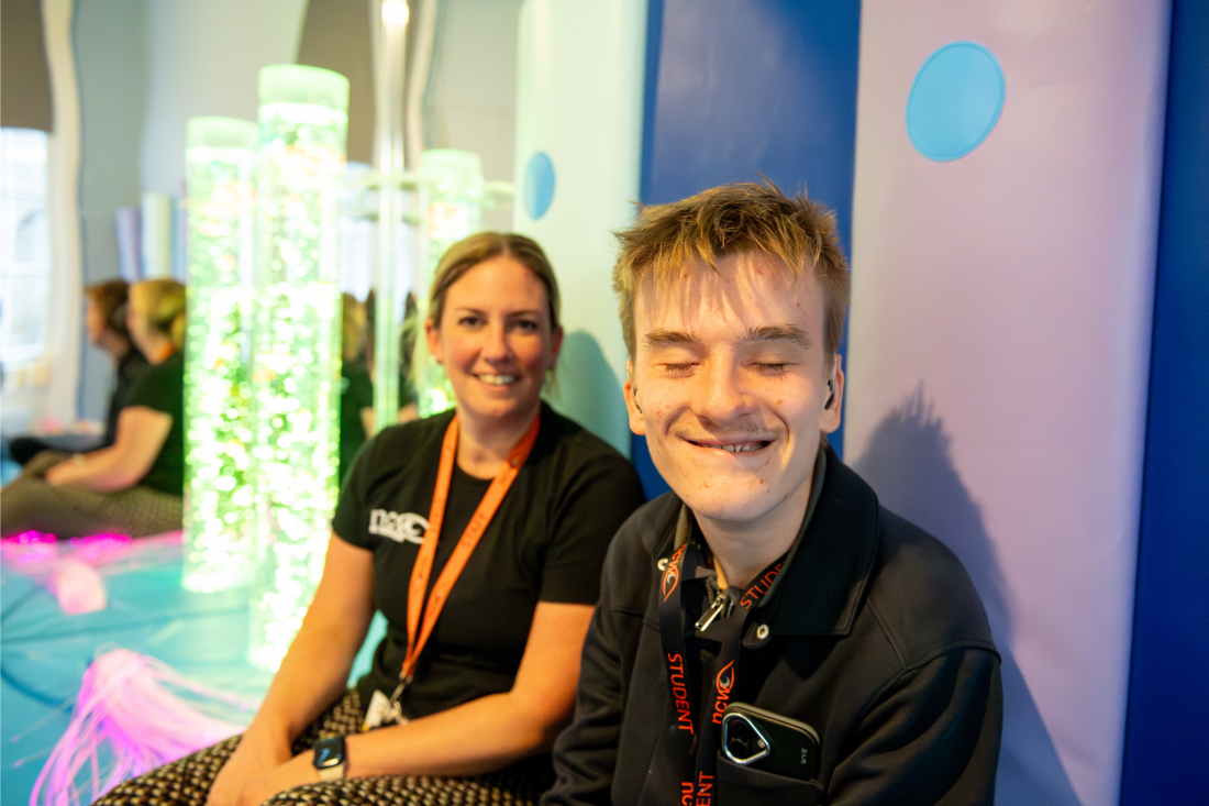 A student smiling whilst sat in a sensory room with a member of staff