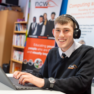 A smiling student in uniform wearing headphone and working on a laptop in a classroom