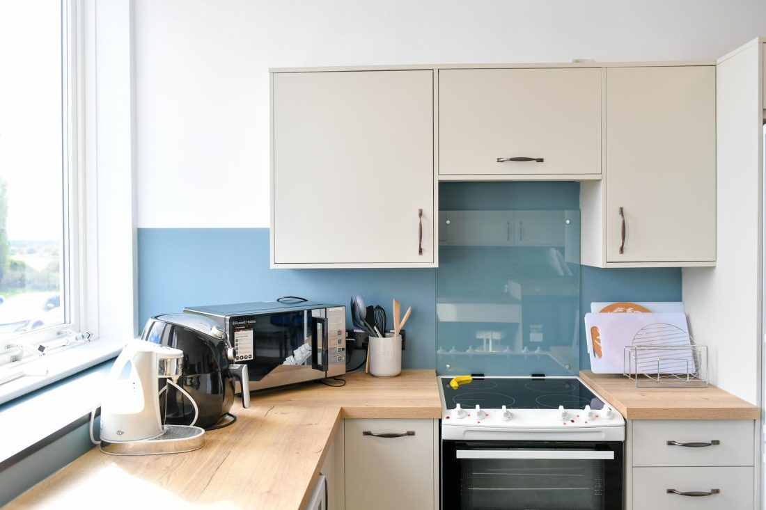 Close-up of the kitchen worktop showing a kettle, accessible measuring jug and microwave against the contrasting blue splashback.