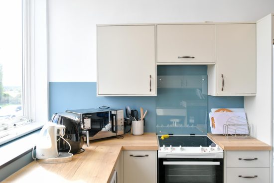 Close-up of the kitchen worktop showing a kettle, accessible measuring jug and microwave against the contrasting blue splashback.