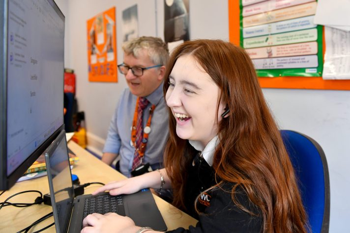 Photo of a student and staff working together at a desk smiling.